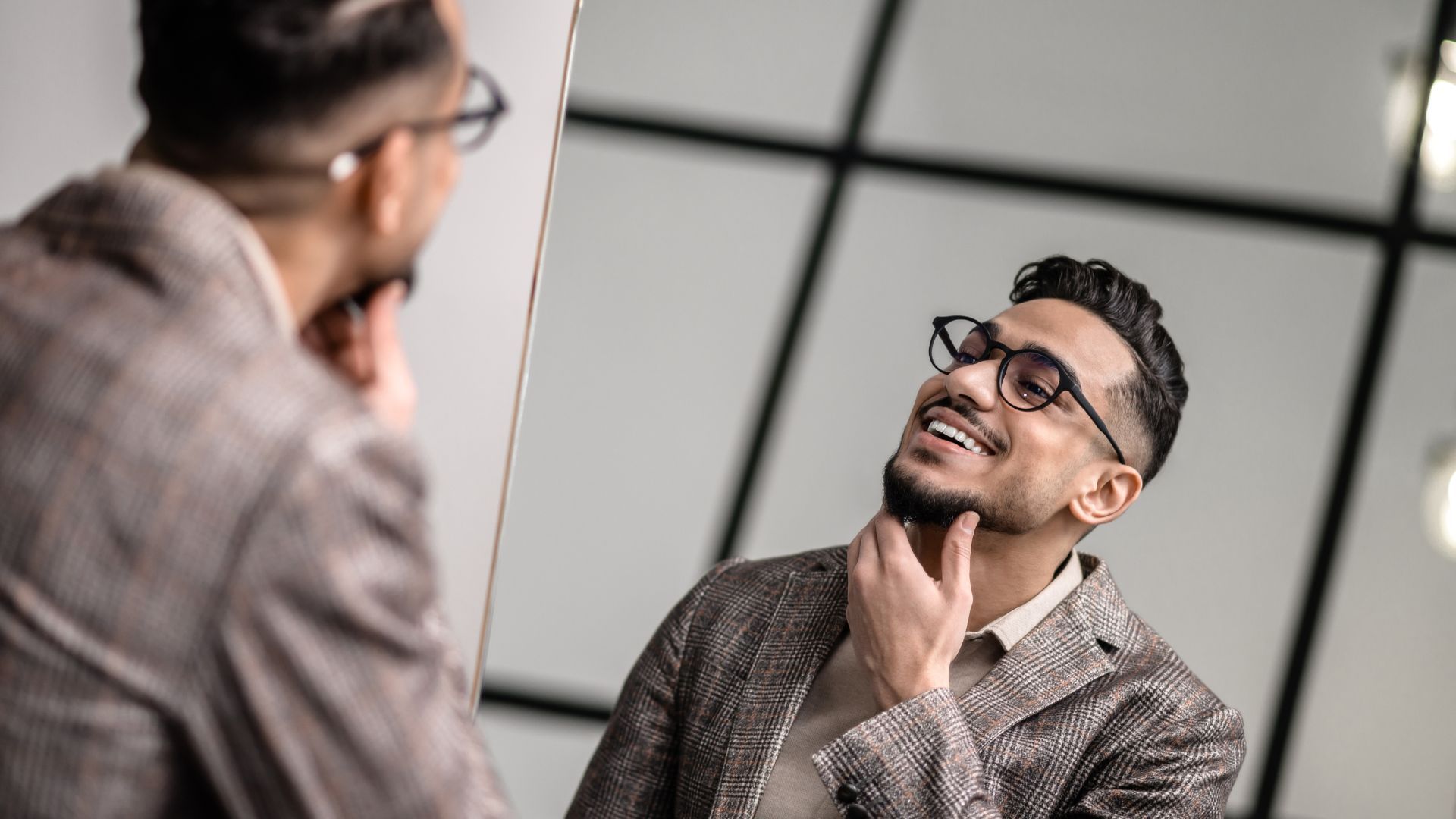 Homme en veste à carreaux souriant et regardant son reflet dans le miroir.